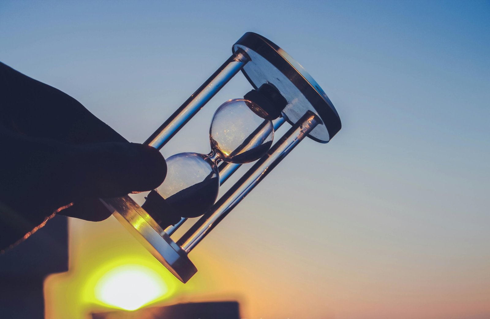 Silhouette of an hourglass held against a vibrant sunset sky in Syria. Time concept.